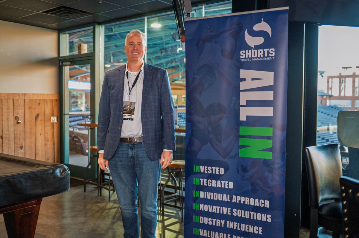Partner representative beside a Shorts Travel Management banner at the ballpark suite